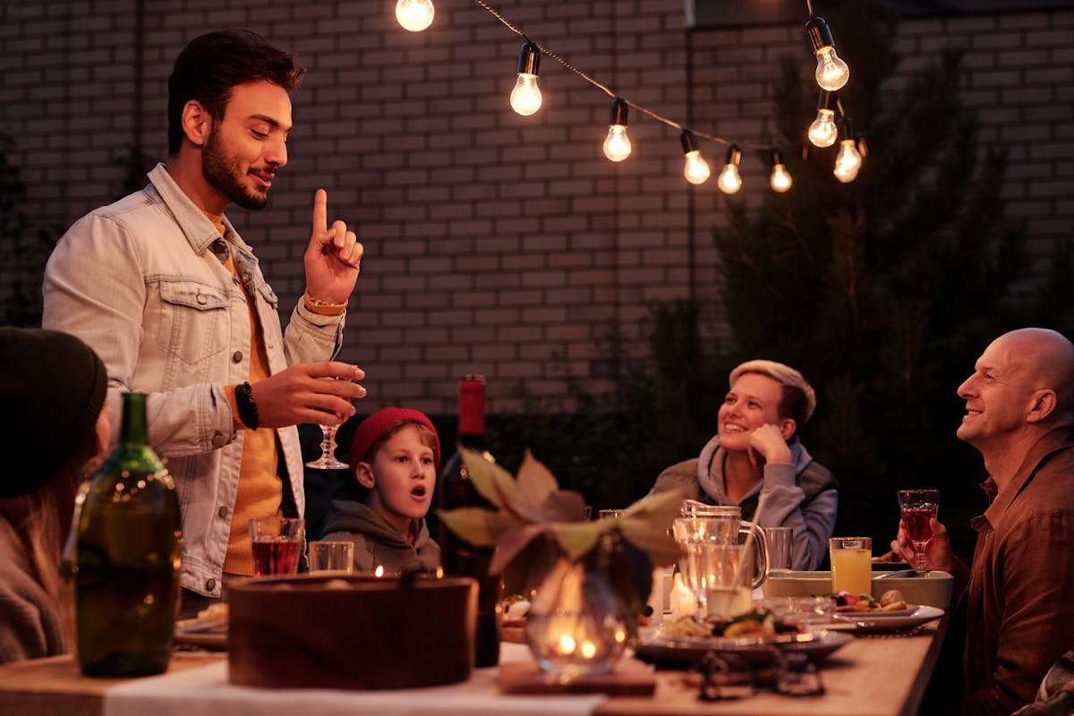 A cheerful group enjoying a festive evening gathering with lights and drinks on a cozy patio garden