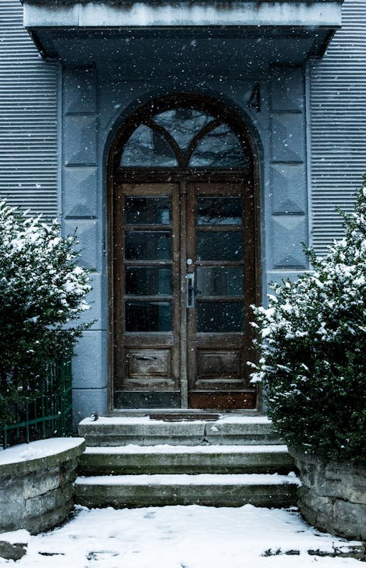 Charming wooden doorway covered in snow with surrounding greenery during winter.
