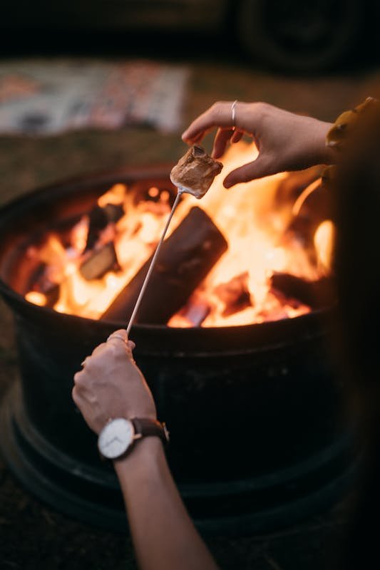 Close-up of hands roasting marshmallows over a campfire, capturing a cozy patio garden evening ambiance.