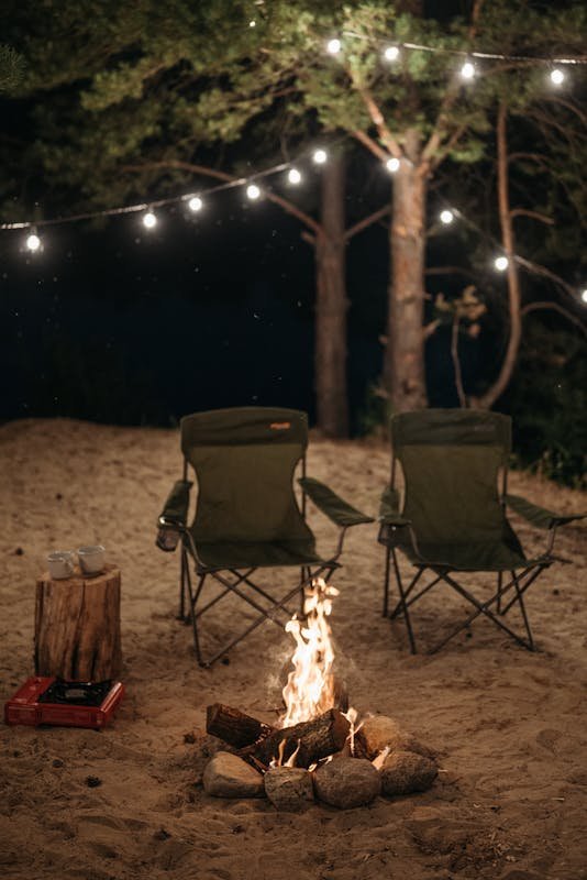 A cozy night scene featuring two chairs by a campfire with string lights. Perfect for outdoor camping themes.